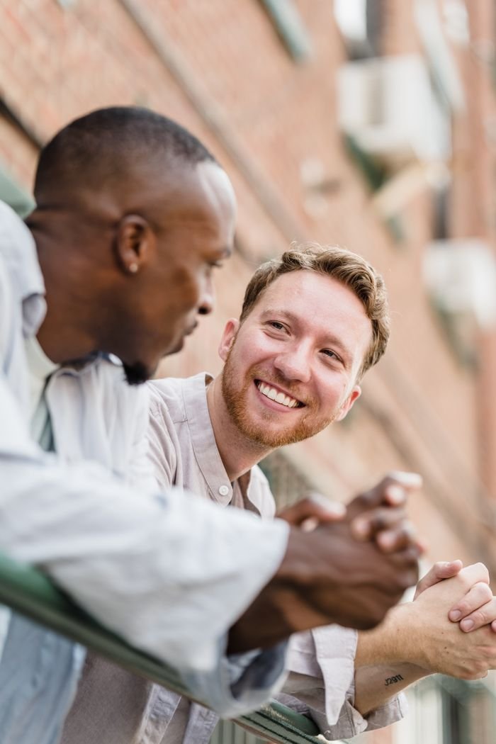 Two men engaging in a cheerful conversation outdoors, smiling and relaxed.
