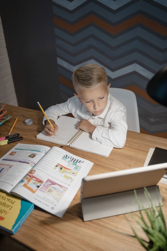 A young boy engaged in learning at home, using a tablet and books on his desk.